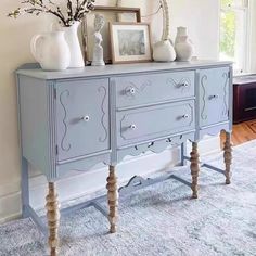 a blue dresser with some vases on top of it in a living room next to a window