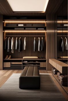 a large walk in closet with lots of clothes hanging on the wall and a bench