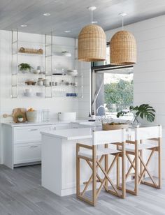 a white kitchen with wooden accents and hanging lights above the island countertop is flanked by two bamboo pendants