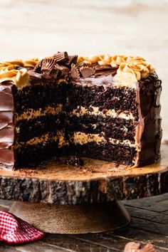 a chocolate cake with one slice cut out on a wooden plate next to a red and white checkered napkin