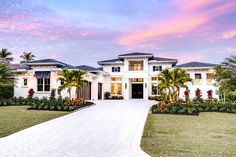 a large white house with palm trees in the front yard and driveway leading to it