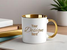 a white and gold coffee mug sitting on top of a desk next to a plant