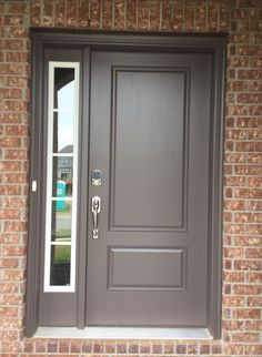 the front door is painted gray and has glass panels on each side, along with a brick wall