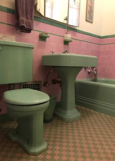 a bathroom with pink and green walls, checkered flooring, and two pedestal sinks