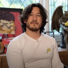 a man with long hair and glasses sitting in front of a desk next to statues