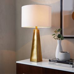 a table lamp sitting on top of a white table next to a book and plant