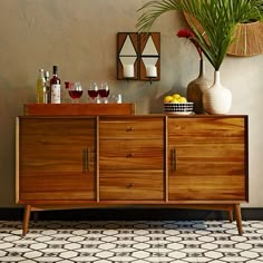 a wooden cabinet sitting next to a vase filled with fruit and wine on top of a tiled floor