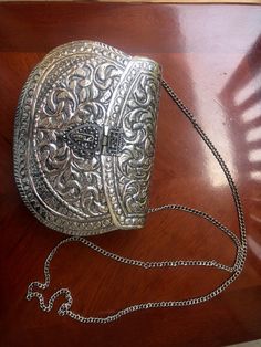 This shoulder purse is made from brass but is a lovely silver antique looking purse with a self design throughout the piece that give it that antique look. There is a front closure on the front of the purse and a metal chain. The inside of the purse is a nice black velvet material that will keep your cell phone and other valuables protected. It is a nice bag for a lunch out or a nice evening paired with a dress or your traditional Indian event. It works well as a unique gift for an art or antiqu Silver Metal Rectangular Shoulder Bag, Silver Rectangular Metal Shoulder Bag, Rectangular Silver Metal Shoulder Bag, Silver Metal Evening Bag As Gift, Silver Rectangular Metal Clutch, Silver Clutch For Wedding And Festivals, Silver Metal Clutch As Gift, Antique Silver Rectangular Evening Bag, Silver Antique Rectangular Evening Bag