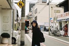 a woman standing on the side of a street next to a traffic light and buildings