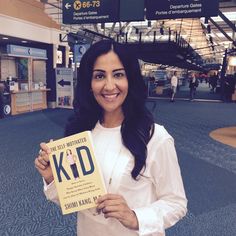 a woman standing in an airport holding up a sign that reads, the safe monitored kid