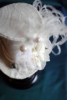 A Mad Hatter fascinator hat with a bridal twist! The hat is covered with beautiful textured ivory brocade and embellished with ivory satin ribbon around the crown. Trimmed with pearl hats pins, ivory roses and hydrangea blossoms,ivory feather spray, the signature 10/6 Mad Hatter card and of course a tiny silver tea-pot! Cause around here it's always tea-time! Both hat pins have push-in clasps to avoid accidents! Veil may be added at an extra cost. This mini top hat is fully lined with satin and White Curved Brim Fascinator For Vintage Events, Elegant White Hat For Vintage Events, Elegant White Costume Hat As Gift, Elegant White Hats For Vintage Events, Elegant White Hat For Gift, Elegant Cream Costume Hats For Vintage Events, Vintage White Mini Hat For Royal Ascot, Vintage White Costume Hat For Formal Occasions, Vintage White Top Hat For Formal Occasions