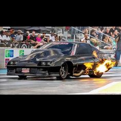 a black car with flames on it driving down the street in front of a crowd