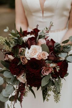 a bridal holding a bouquet of red and pink flowers with greenery on it