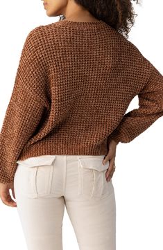 a woman wearing a brown sweater and white pants