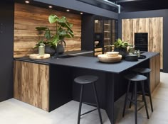 a kitchen with black counter tops and stools next to a plant on the island