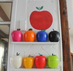 there are many different colored apples on the shelves in front of each other with one apple painted on it