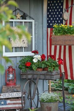 an old wagon filled with flowers and potted plants in front of a flag on the side of a building