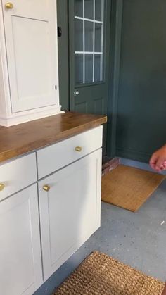 a person standing in front of a kitchen counter with a brown door mat on the floor