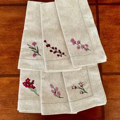 four embroidered napkins with flowers on them sitting on a wooden table next to each other