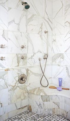 a bathroom with marble walls and flooring has a bathtub, shower head, and hand held faucet