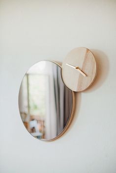 a round mirror mounted to the side of a wall with a wooden clock on it