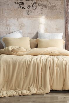 an unmade bed with beige sheets and pillows on it in front of a brick wall