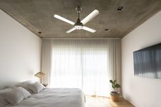 a bedroom with a large bed and ceiling fan in the corner next to a flat screen tv