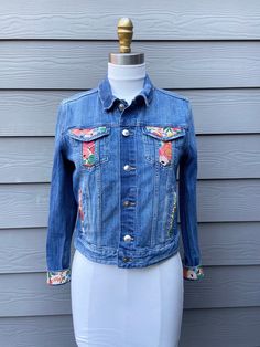 a blue jean jacket with colorful patches on the front and back, sitting on a mannequin