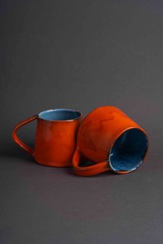 two orange mugs sitting next to each other on a gray surface, one is empty