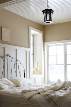 an unmade bed in a bedroom with two windows and a lamp hanging from the ceiling