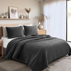 a bedroom with a large bed covered in grey blankets and pillows next to a window