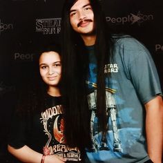 a man with long hair standing next to a woman