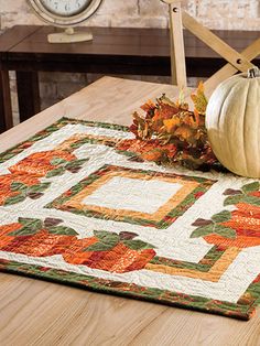 a quilted placemat with a pumpkin on it next to a wooden chair and clock