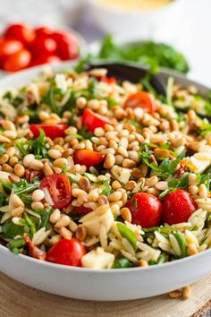 a salad with tomatoes, spinach and pine nuts in a white bowl on a wooden table