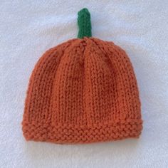 an orange knitted pumpkin hat laying on top of a white blanket with a green tip