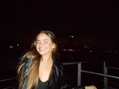 a woman standing next to a fence at night with her hair blowing in the wind