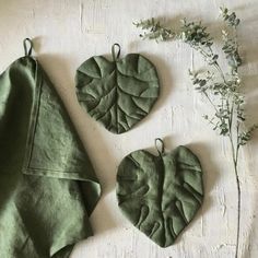 three pieces of cloth with leaves hanging from them on a white surface next to a plant