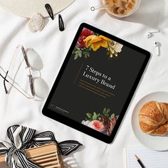 the 7 steps to a luxury brand book is displayed on an ipad next to coffee and croissants