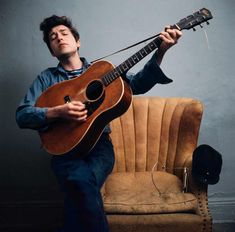 a man sitting on a chair holding an acoustic guitar