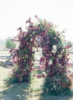 an arch made out of vines and flowers on the grass in front of a wooden fence