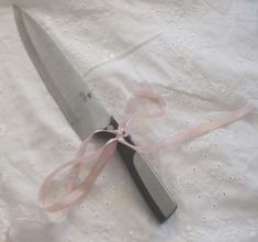 a pink ribbon tied around a knife on top of a white tablecloth with lace