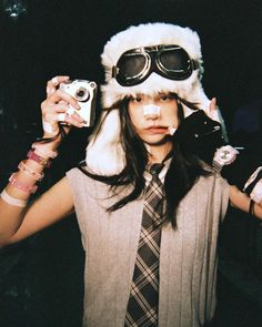 a woman with long hair wearing a hat and goggles holding two camera's