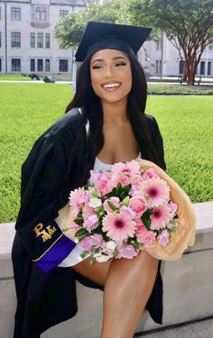 a woman in graduation cap and gown holding a bouquet of flowers sitting on a bench