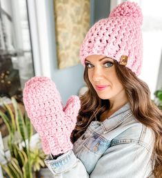 a woman wearing a pink knitted hat and mittens with her hands in the air