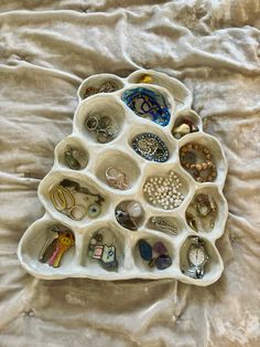 a white tray filled with lots of different types of jewelry on top of a bed