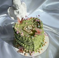 a green cake with flowers and an angel decoration on top, sitting on a white table cloth