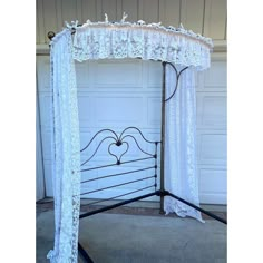 an iron bed frame with white lace on it and a heart at the top, in front of a garage door