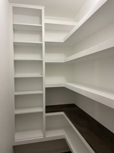 an empty closet with white shelves and wood flooring