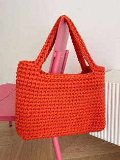 an orange crocheted bag sitting on top of a pink chair next to a radiator