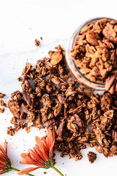 a bowl full of granola next to flowers on a white surface with an orange flower